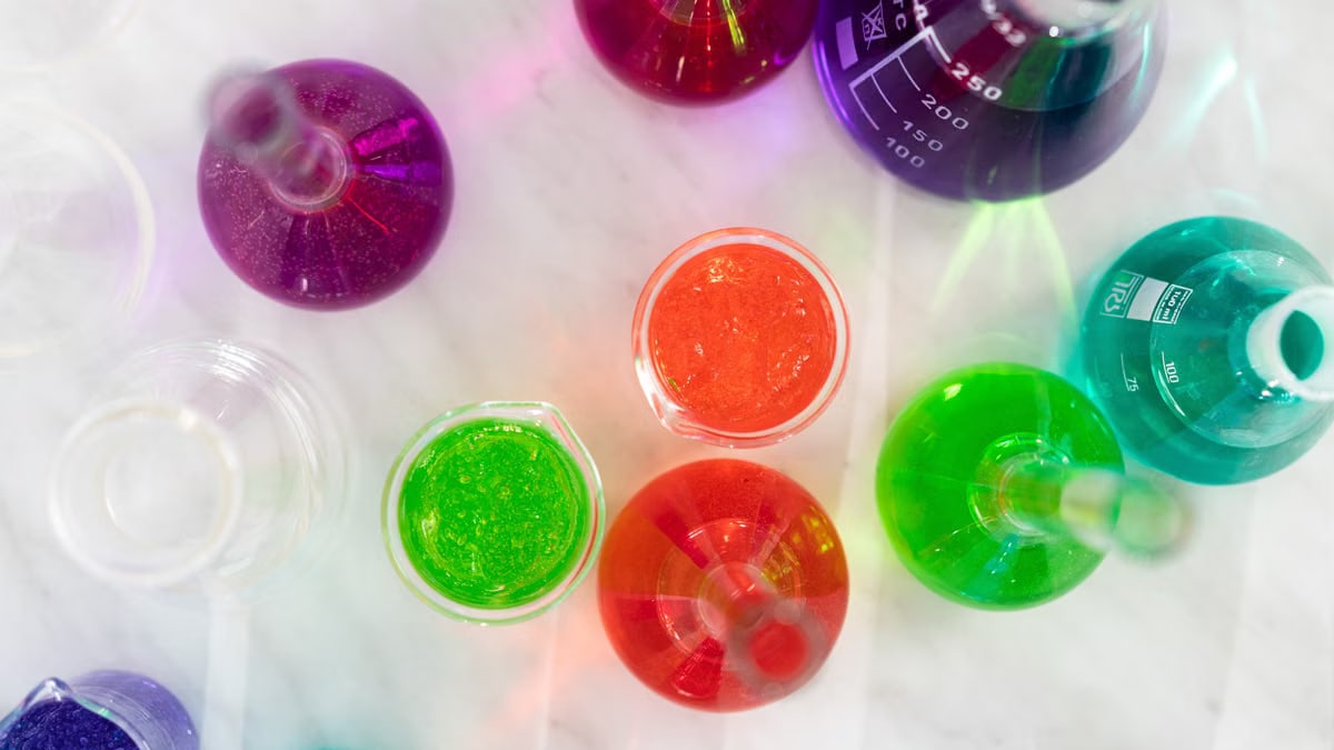 Aerial view of colorful liquids in laboratory glassware on marble surface, showcasing vibrant hues.